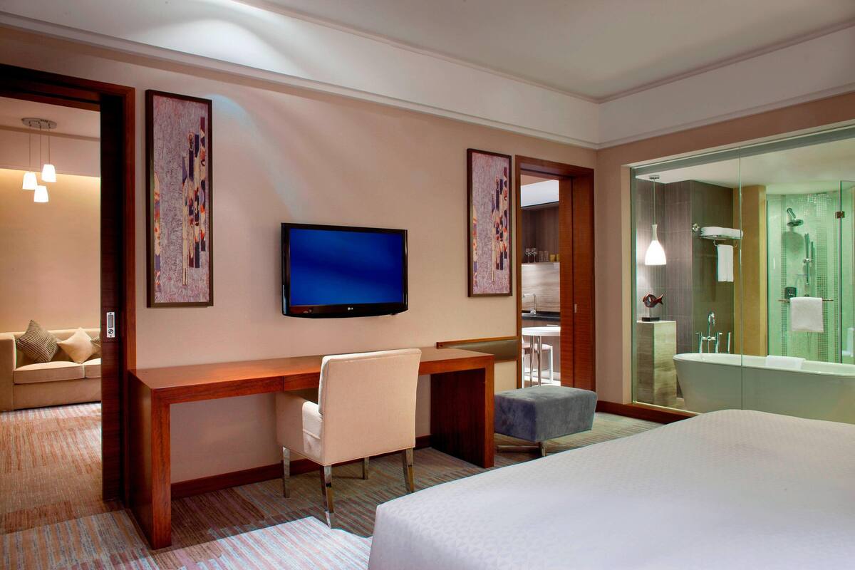 A hotel room with a bed, a desk with a chair, a television, and a bathroom with a bathtub and shower.