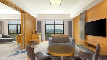 A modern hotel room with a large window, a flat-screen TV, a round table, and a sofa.