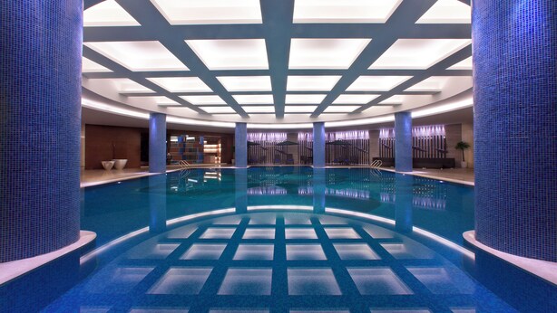 Ein großes Hallenbad mit Fliesenboden und -decke, umgeben von blauen Fliesenwänden und Säulen.