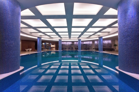 A large indoor swimming pool with a tiled floor and ceiling, surrounded by blue-tiled walls and columns.