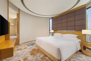 Habitación de hotel moderna con una cama grande, televisión, baño y vistas a la ciudad.