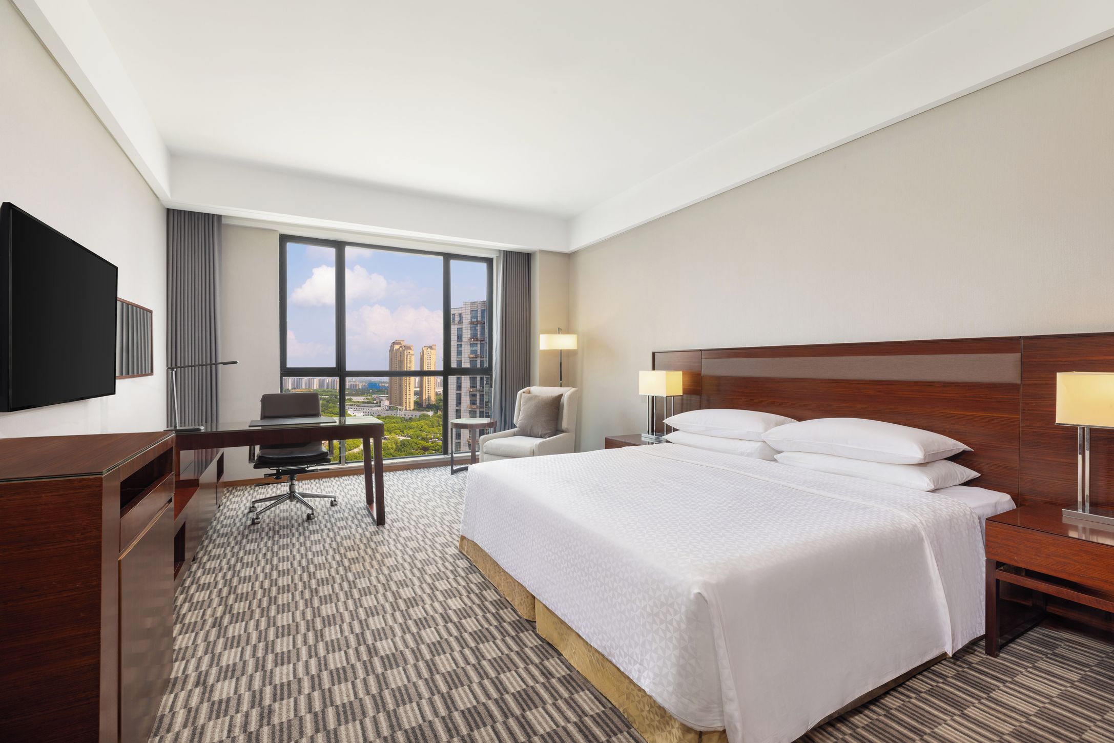 Une chambre d’hôtel avec un grand lit, un bureau, une chaise, une télévision et une vue sur le paysage urbain.