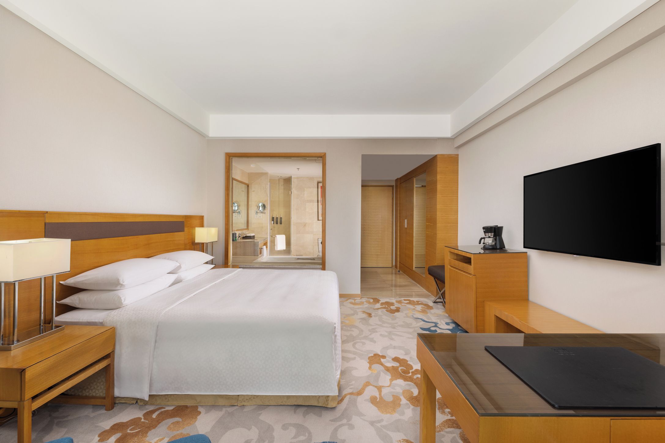 A hotel room with a bed, bedside tables, a desk, a flat-screen TV, and a shower area.