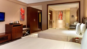 Ein Hotelzimmer mit zwei Betten, einem Schreibtisch, einem Fernseher und einem Badezimmer mit Dusche und Toilette.