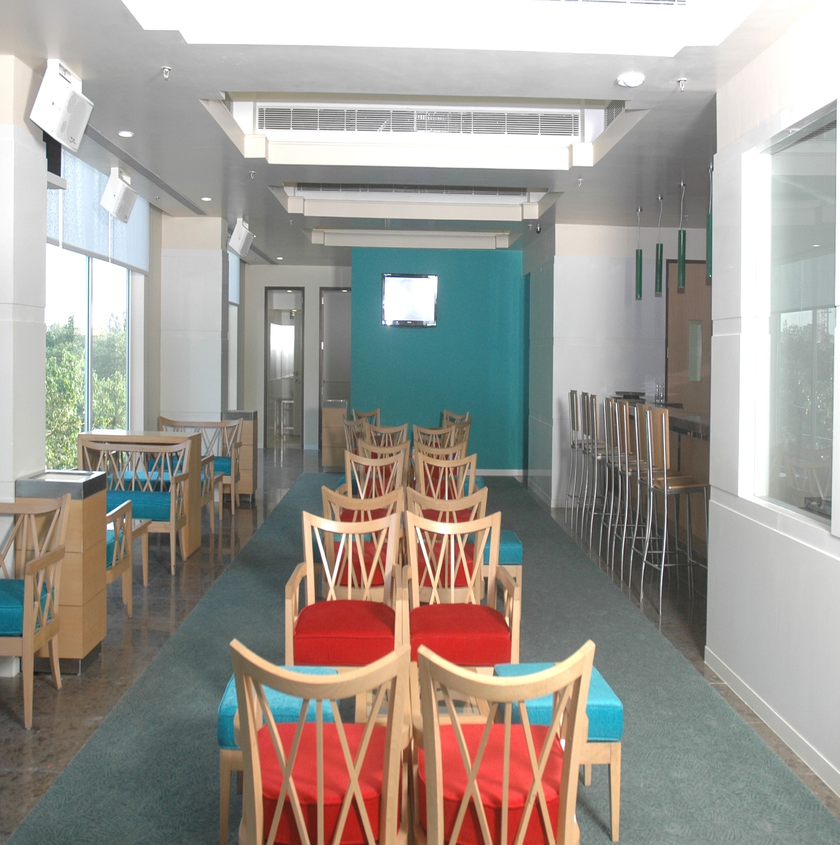A modern dining area with wooden chairs and tables, large windows, and a teal accent wall.