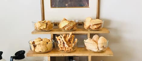 A wooden serving tray with various food items, including crackers, bread, and pastries, displayed on a table.