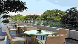 An outdoor seating area with wicker furniture and glass tables, surrounded by greenery and a glass railing. - Hometel Chandigarh (Chandigarh)