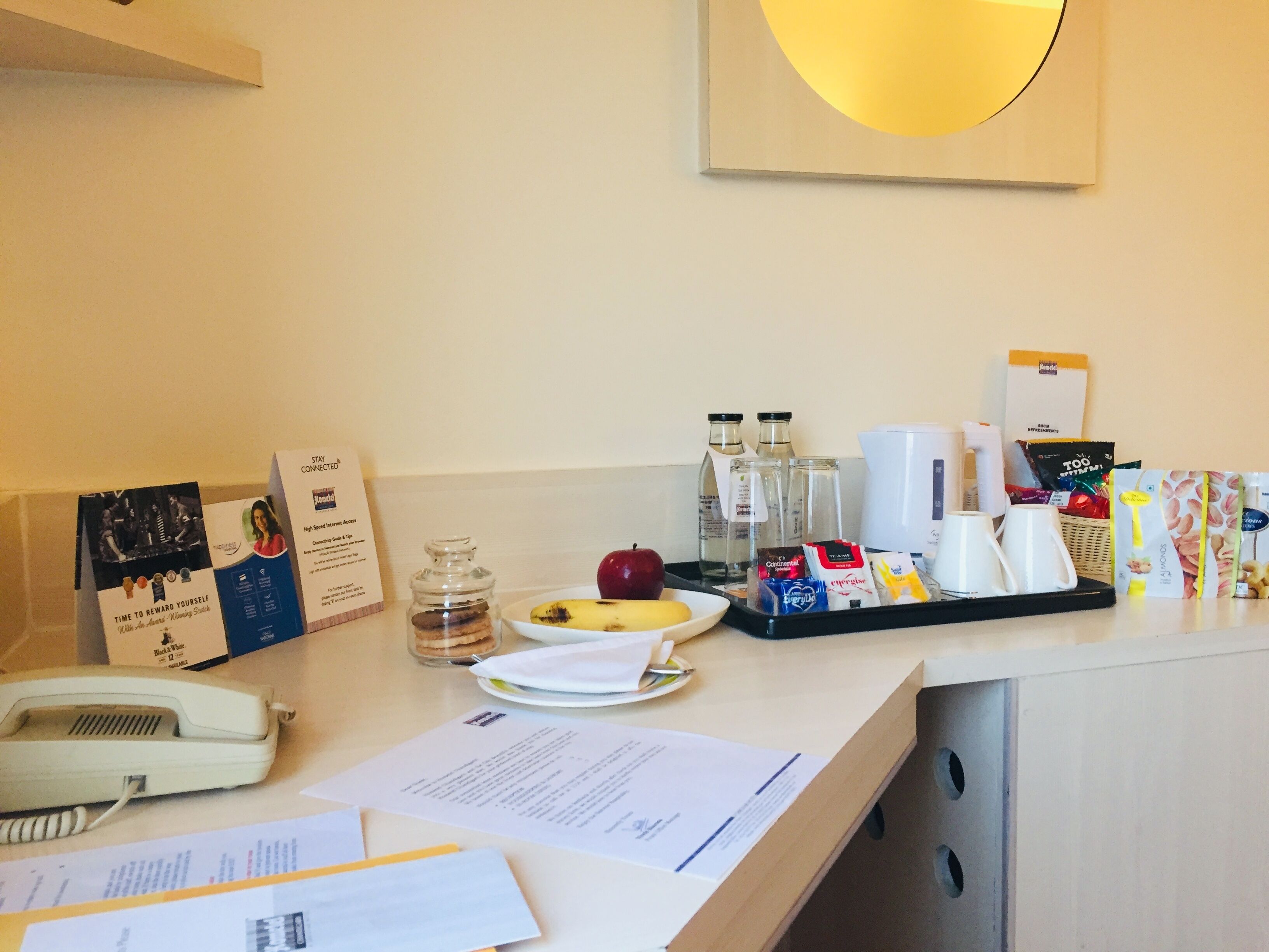 En hotellreception med en telefon, papper, en tallrik med frukt och diverse bekvämligheter som kaffe, te och snacks.