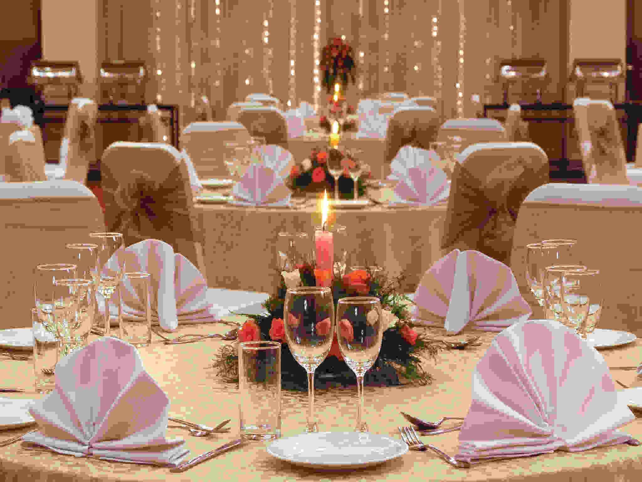 A formal dining setup with round tables, white tablecloths, and pink fan-shaped napkins.