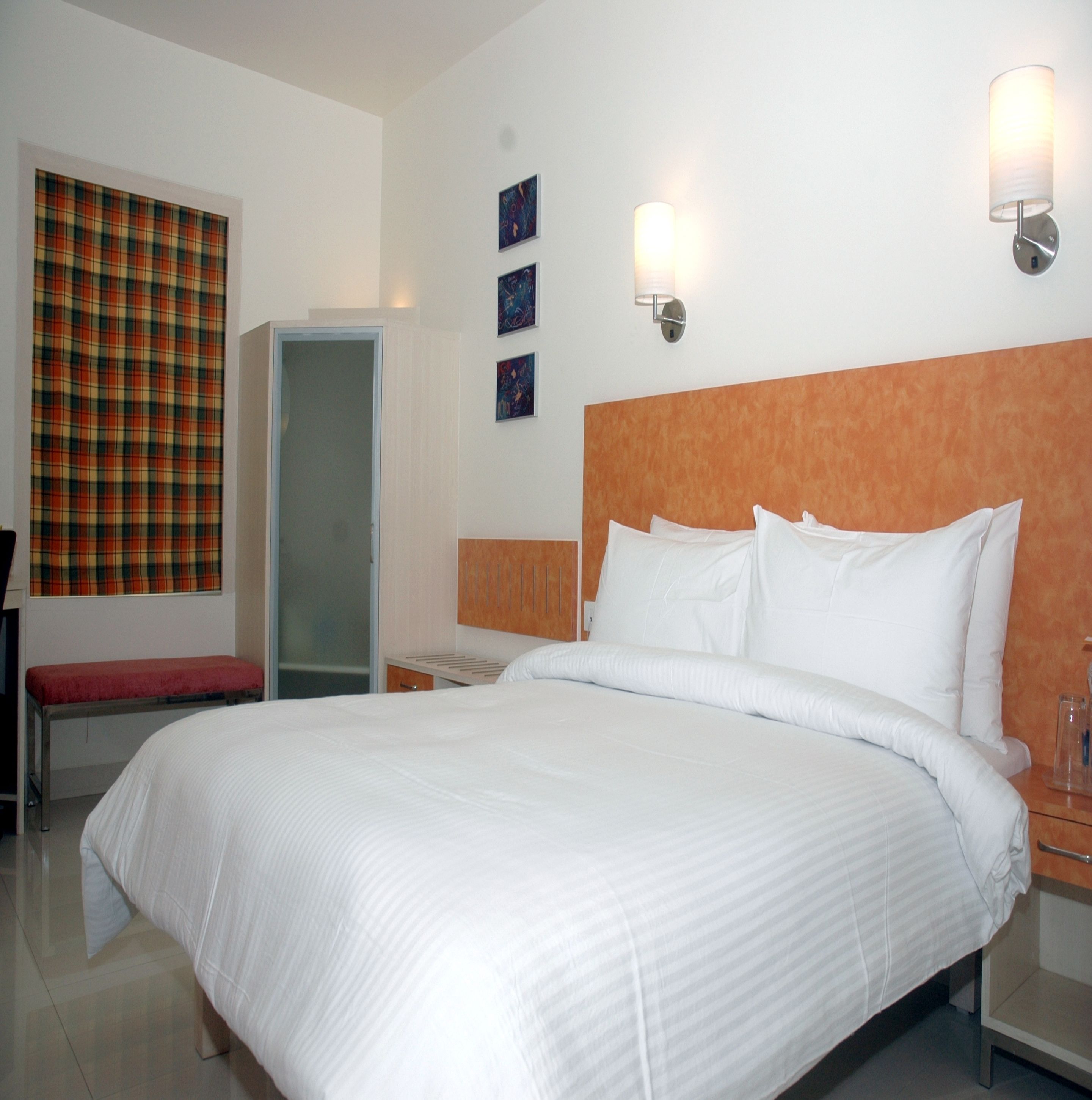 A hotel room with a large bed, a bench, a wardrobe, and a door.