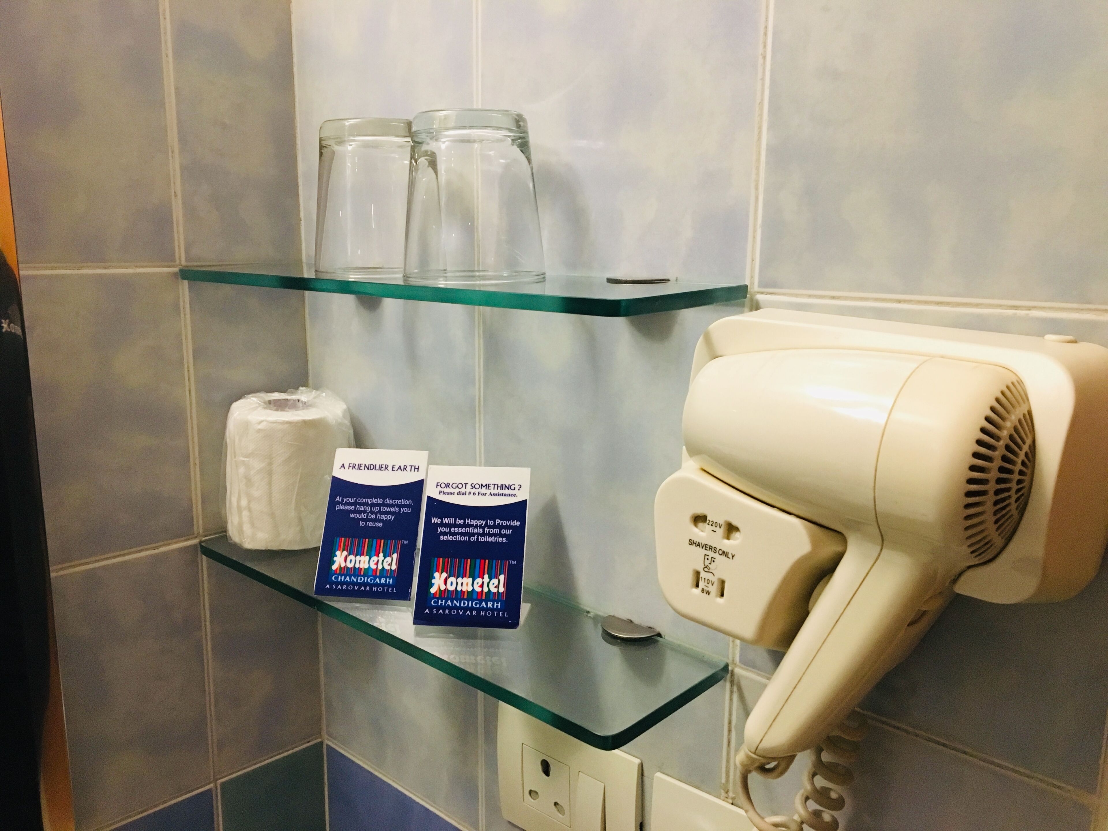Un baño con repisas de vidrio que sostienen artículos de tocador, un secador de pelo y dos cajas de pañuelos.