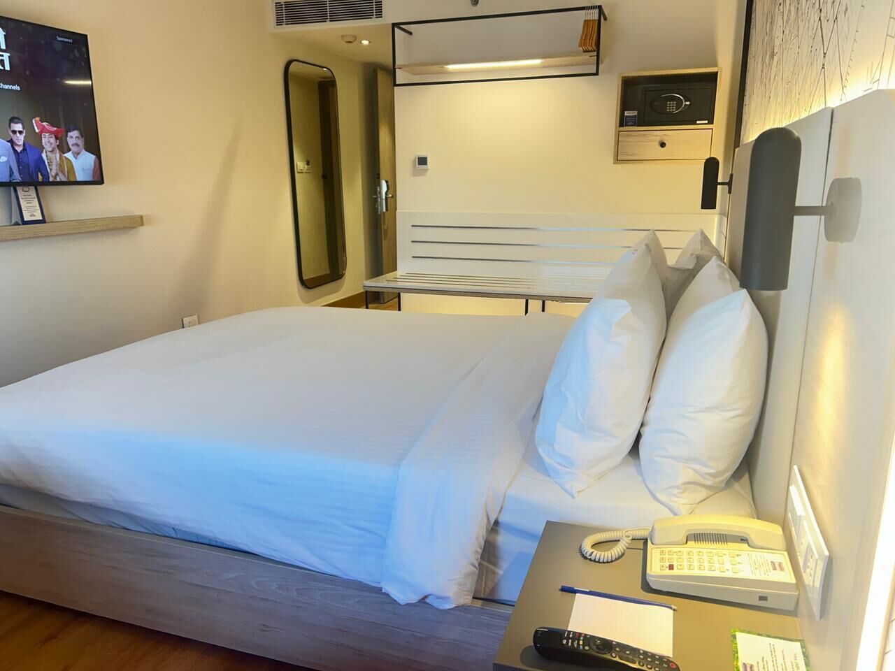 Une chambre d’hôtel avec un lit, une table de chevet et un téléviseur fixé au mur.