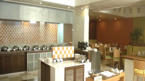 A modern hotel kitchen with a central island, a dining area with tables and chairs, and a patterned wall. - Hometel Chandigarh (Chandigarh)