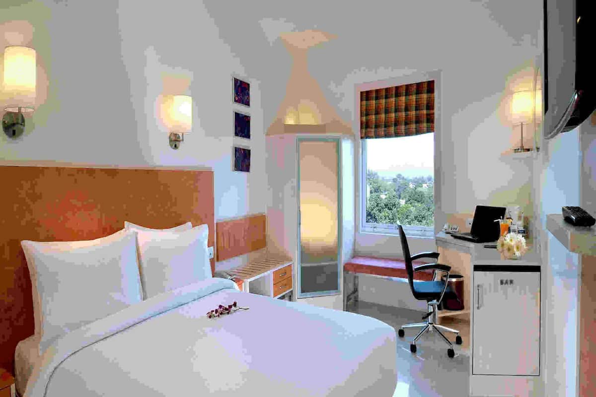 Une chambre d’hôtel avec un lit, un bureau, une chaise, une télévision et une fenêtre donnant sur un beau paysage.
