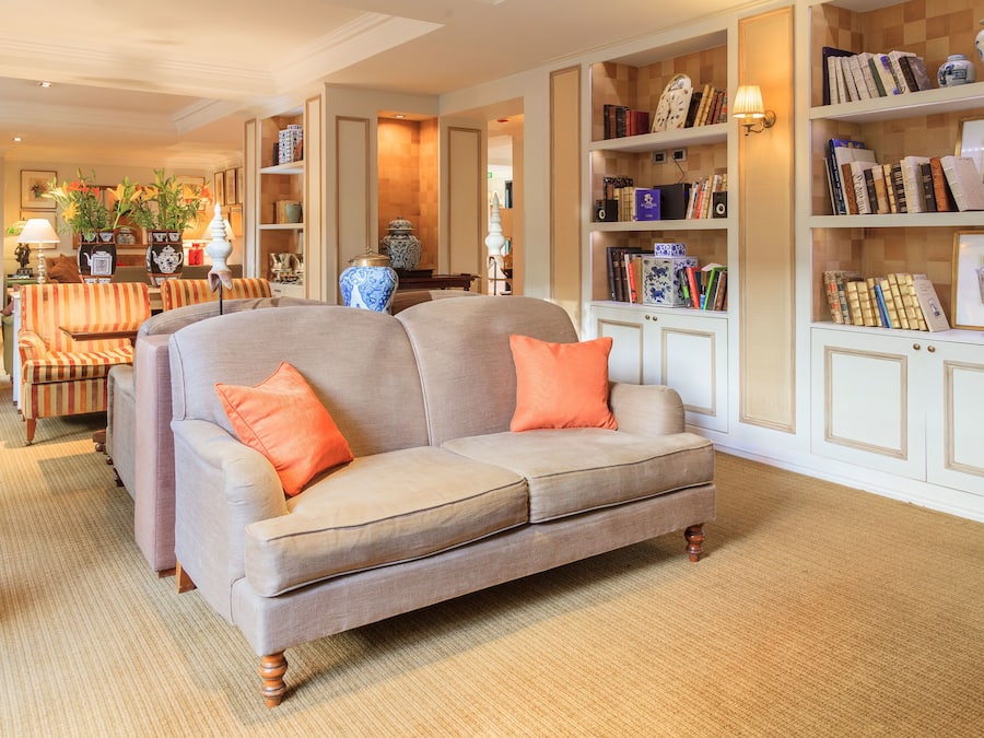 Una sala de estar con un sofá color beige, sillones a rayas y una estantería llena de libros y objetos decorativos.