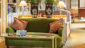 A green sofa with patterned cushions, a glass coffee table, and two vases with flowers.