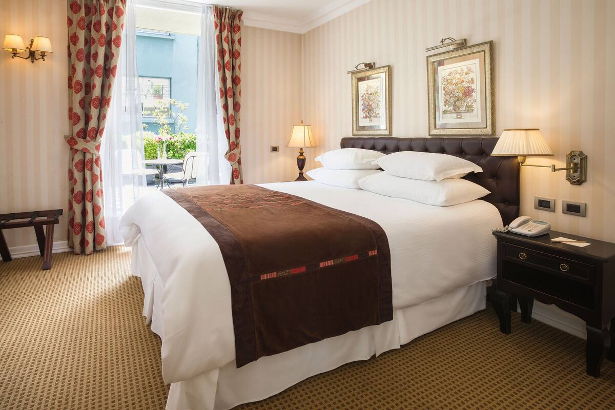 Hotelkamer met een groot bed, twee bedlampjes, een nachtkastje met telefoon en een raam met gordijnen.