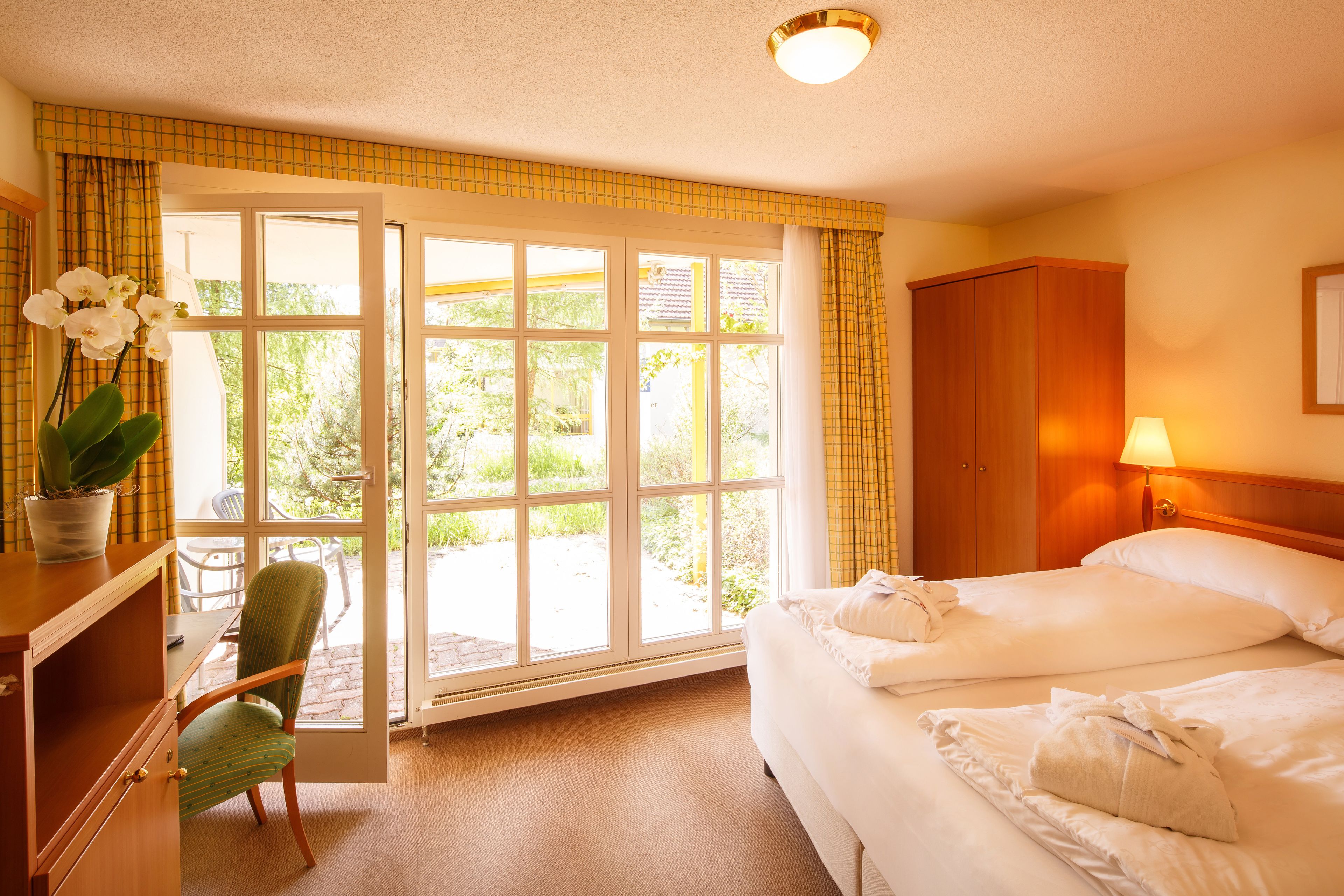 A hotel room with a bed, a chair, a desk, a lamp, and a view of the outdoors through a large window.