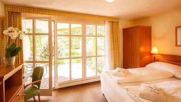 A hotel room with a bed, a chair, a desk, a lamp, and a view of the outdoors through a large window.
