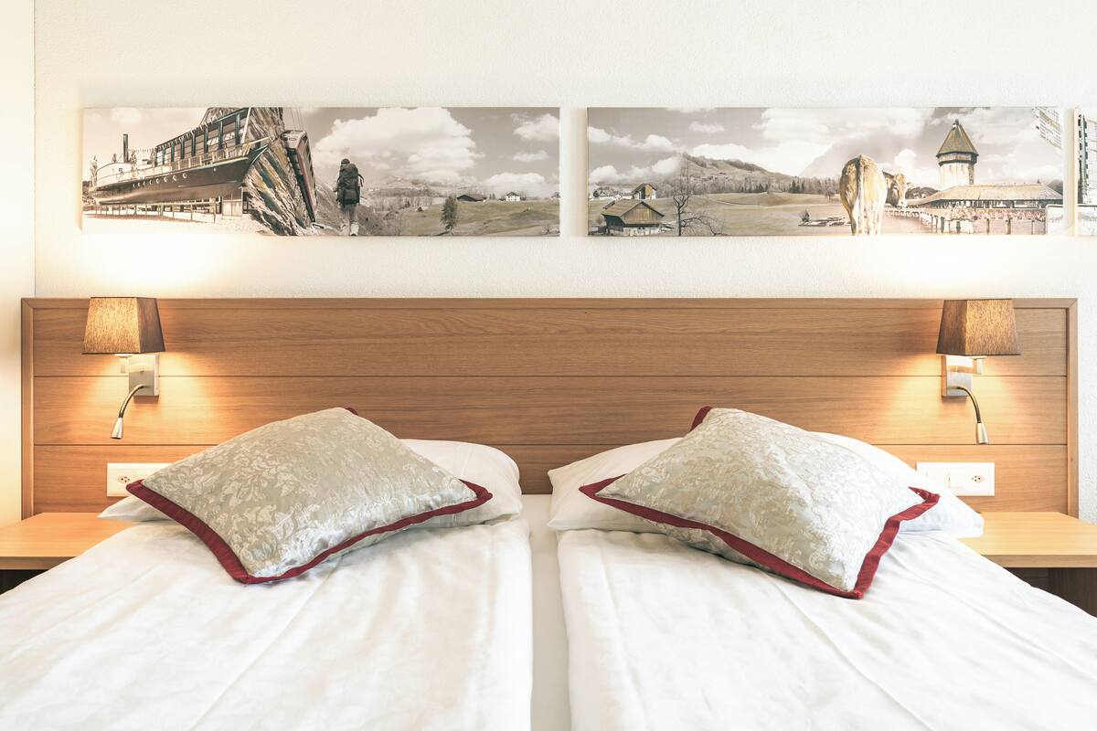 Ein Hotelzimmer mit zwei Betten, einem hölzernen Kopfteil und einem großen Landschaftsbild darüber.