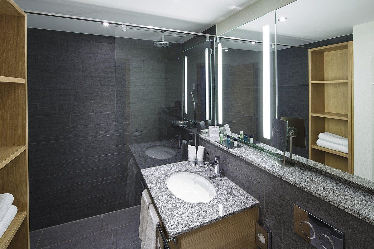A modern bathroom with a granite countertop, a large mirror, a glass-enclosed shower, and a wooden vanity.