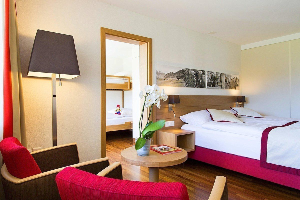 A hotel room with a bed, a desk, a chair, a lamp, and a painting on the wall.