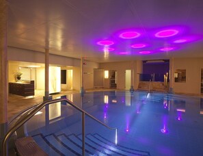 An indoor swimming pool with a staircase leading to a door, surrounded by walls and a ceiling with circular lights. - Swiss Holiday Park Resort (Morschach)