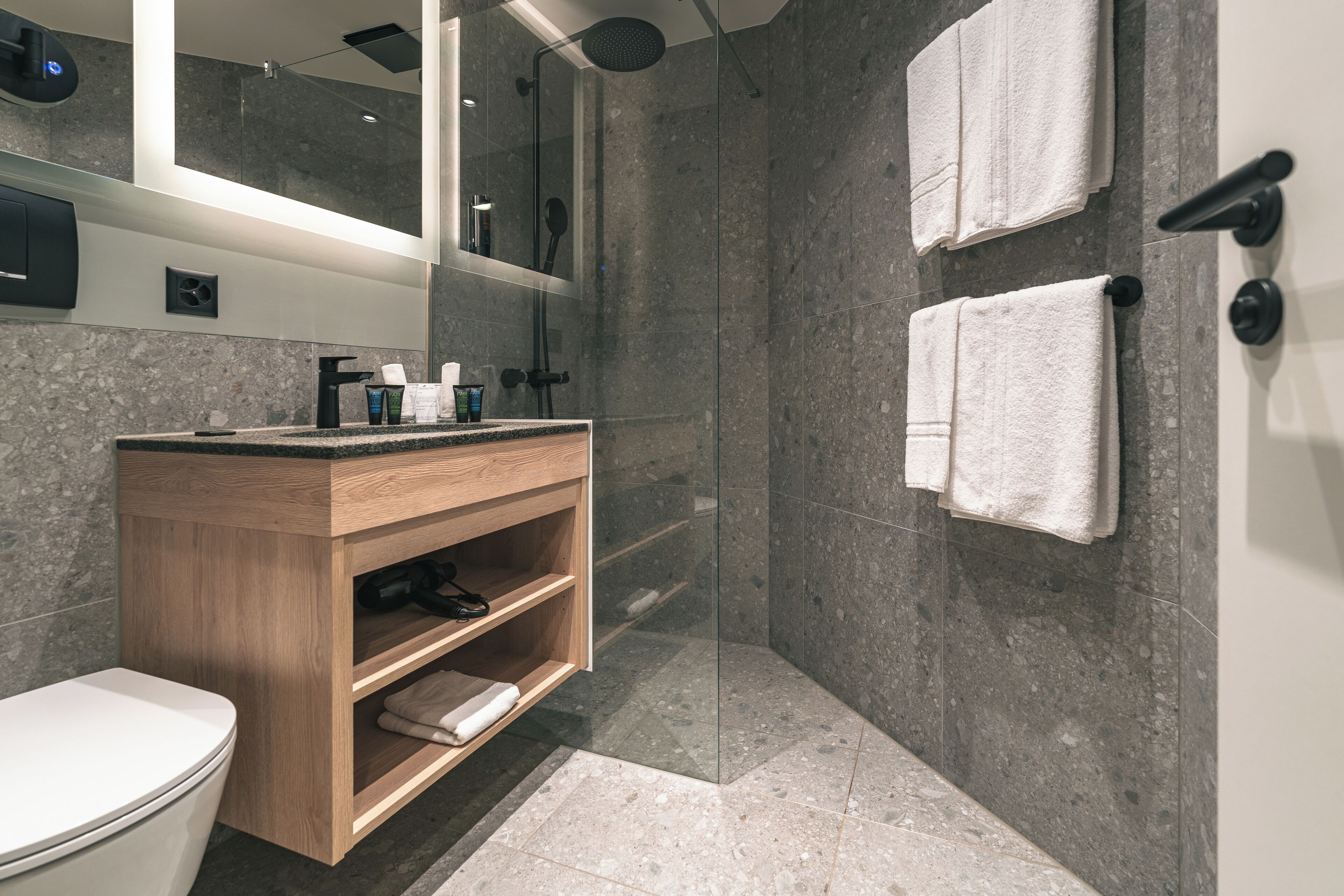 Une salle de bain moderne avec une douche à parois de verre, un meuble-lavabo en bois et deux serviettes blanches accrochées au mur.
