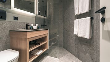 Uma casa de banho moderna com chuveiro de vidro, toucador de madeira e duas toalhas brancas penduradas na parede.