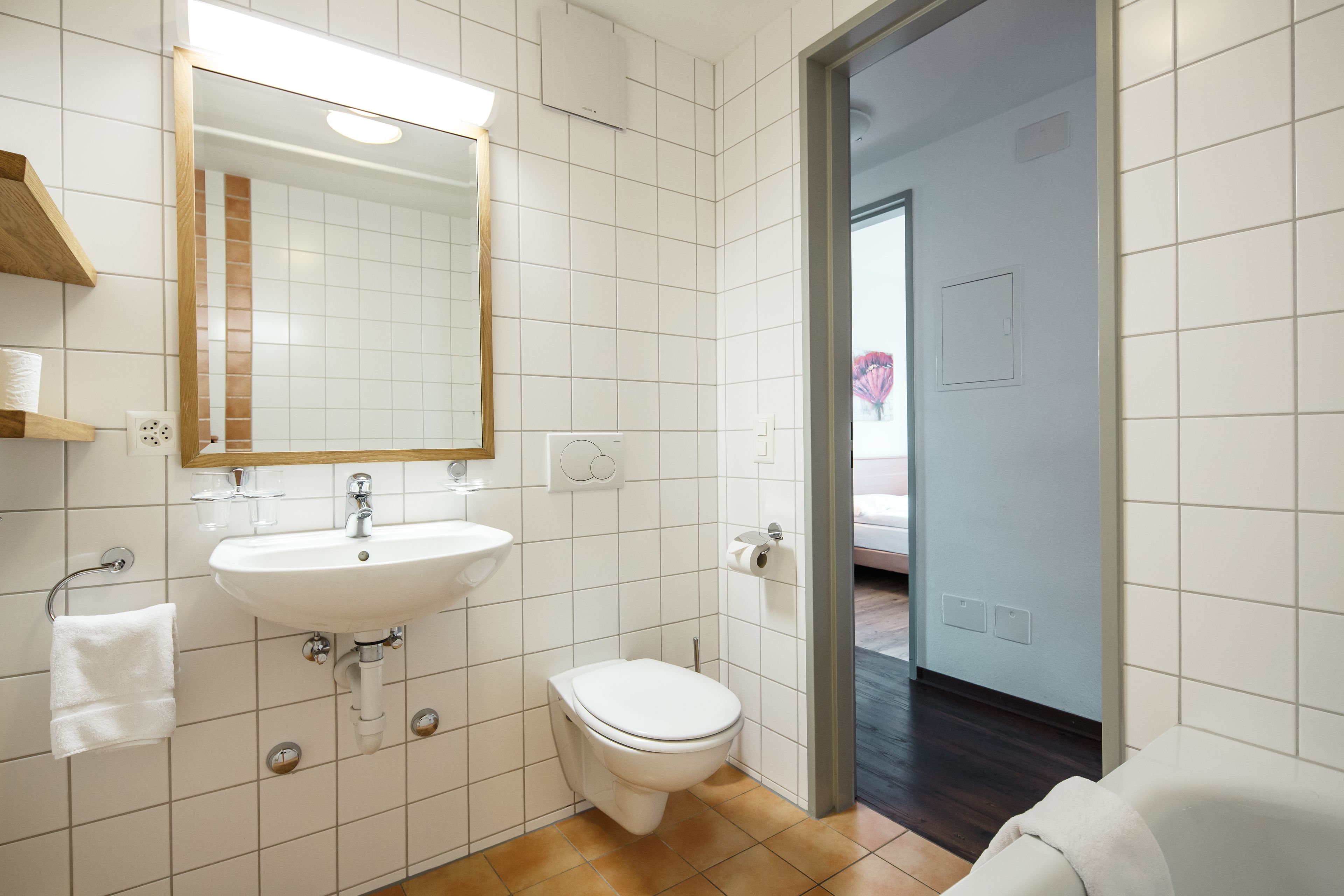 Un baño moderno con azulejos blancos, un lavamanos, un inodoro y un espejo.