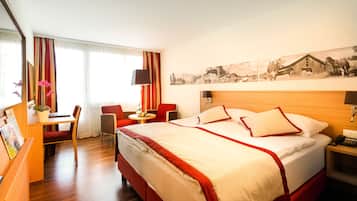 Une chambre d’hôtel avec un grand lit, un bureau avec une chaise, une petite table avec une lampe et un cadre photo posé sur le bureau.