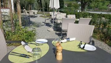 Un espace de restauration en plein air, avec des chaises et des tables en osier, entouré de verdure et offrant une vue sur une colline.