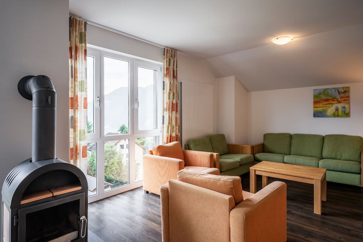 Ein Wohnzimmer mit Kaminofen, grünen Sofas und einem Holztisch.
