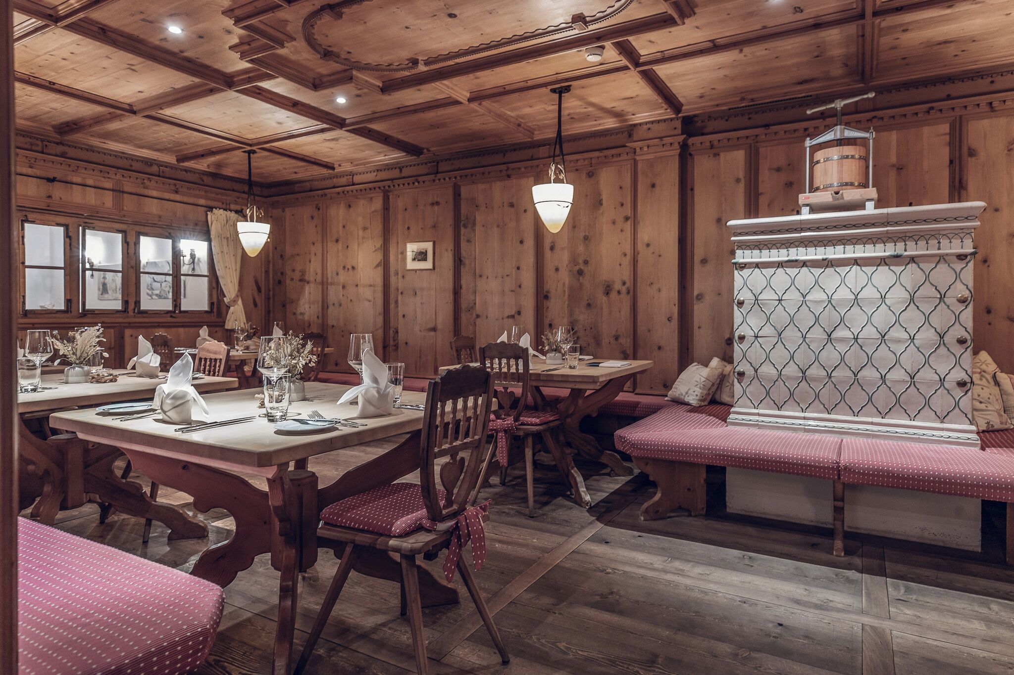L’intérieur est en bois et comprend une table à manger pour quatre personnes, entourée de chaises en bois avec des coussins rouges. Un banc avec un coussin à motifs se trouve au centre.