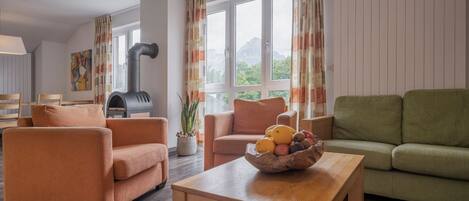 Ein modernes Wohnzimmer mit Kamin, orangefarbenen und grünen Sofas, einem Holztisch und einem Fenster mit Vorhängen.