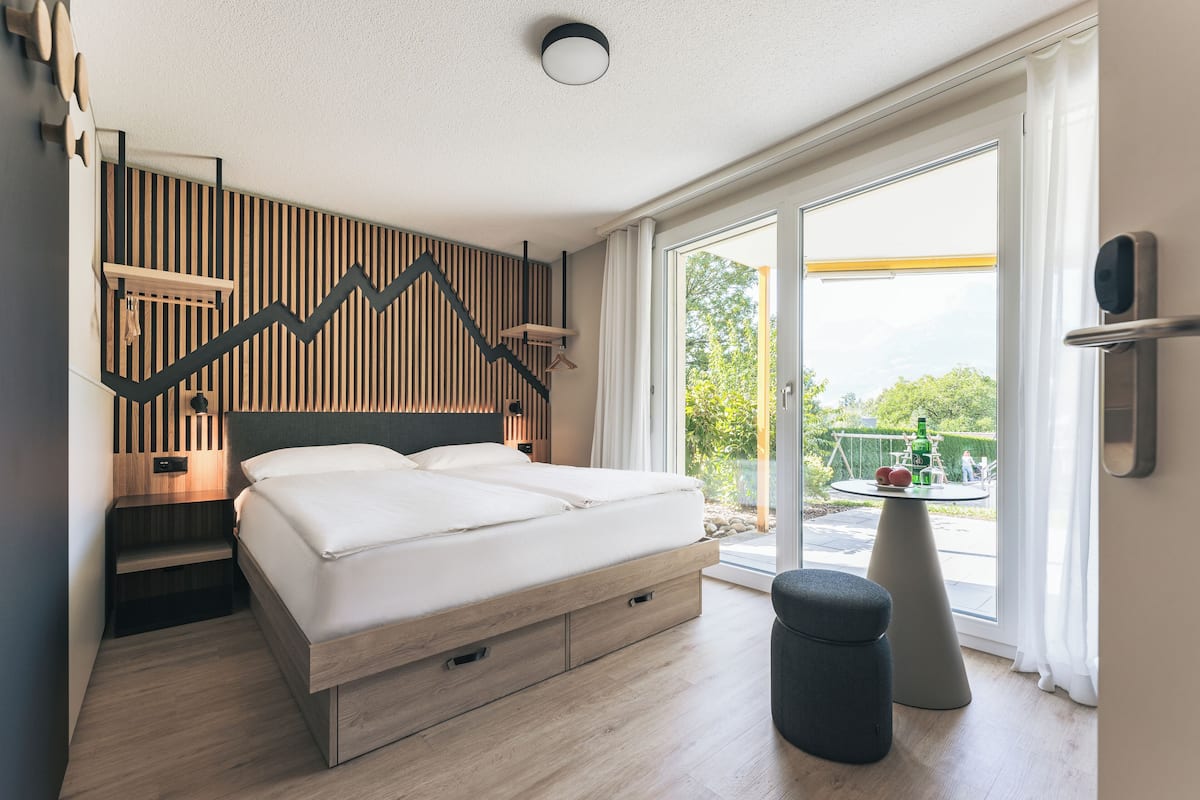 Ein modernes Schlafzimmer mit einem Bett, einer Holzwand und Blick ins Freie.