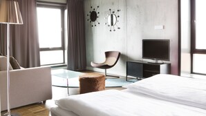 A modern hotel room with a large bed, a flat-screen TV, a round ottoman, a modern chair, and a large window with curtains. - Comfort Hotel Square (Stavanger)