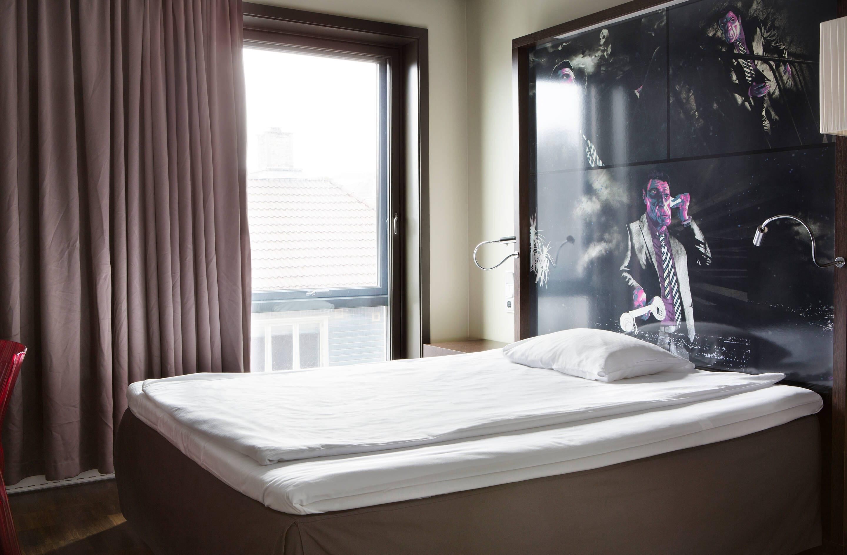 Una habitación de hotel con cama, ventana con cortinas y una pared grande decorada con un mural.