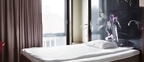 Una habitación de hotel con cama, ventana con cortinas y una pared grande decorada con un mural.