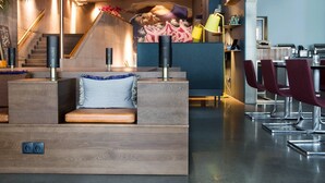 Un vestíbulo moderno con un mostrador de recepción de madera, una zona de estar con cojines azules y una escalera que sube a un nivel superior.