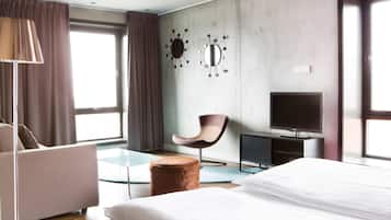 A hotel room with a bed, a desk with a television, a chair, and a large window with curtains.