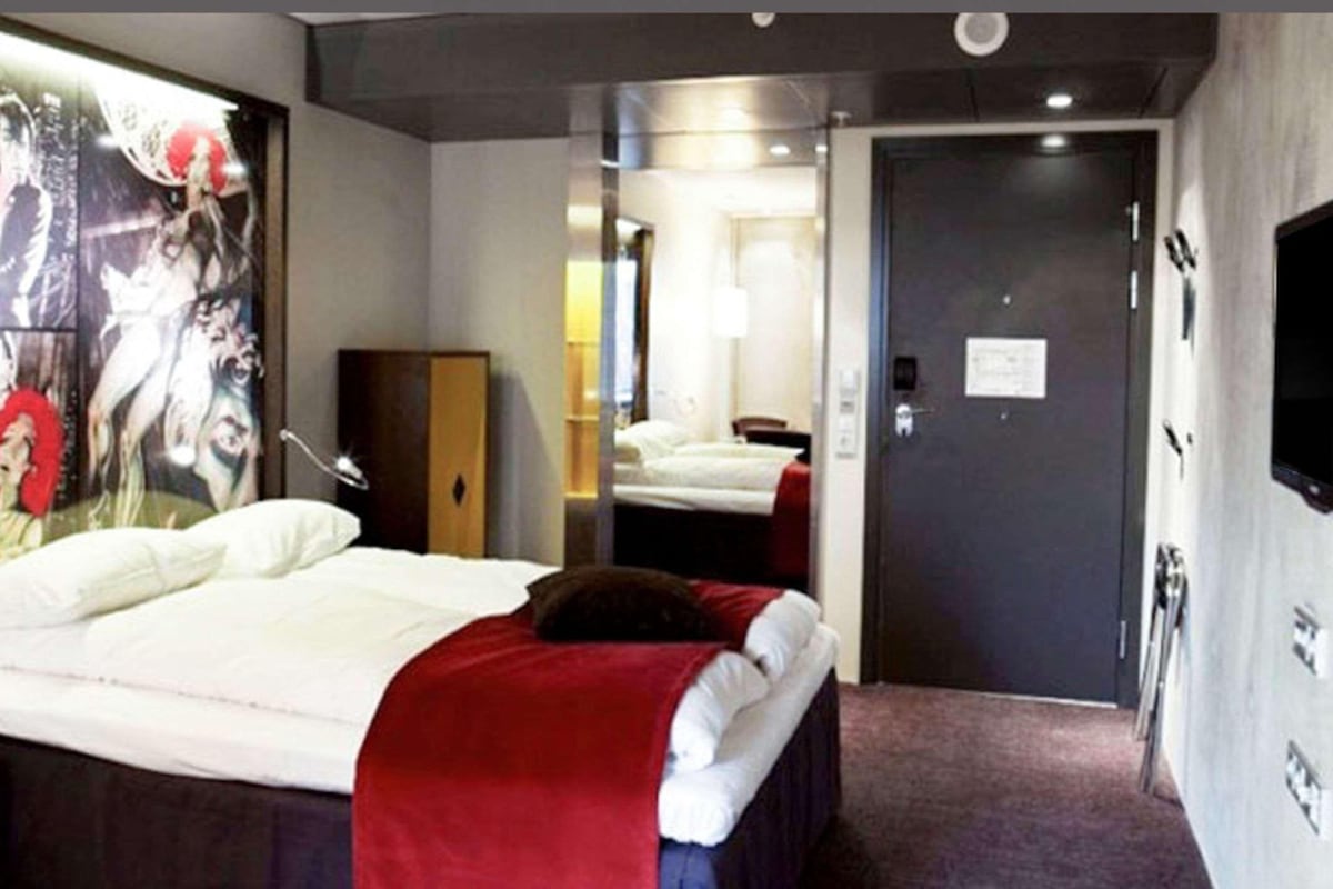 Una habitación de hotel con cama, espejo, armario y televisor.