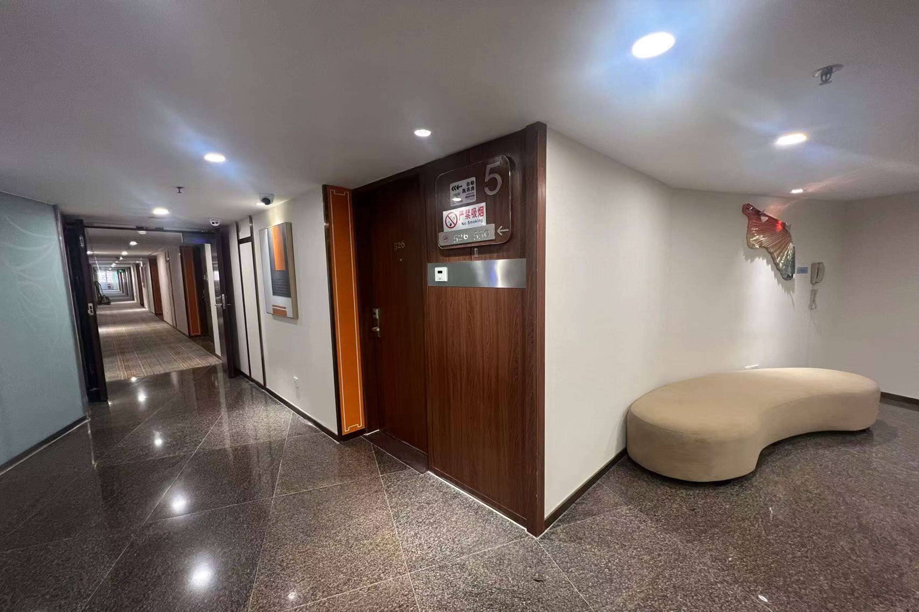 Ein Hotelkorridor mit einer Holztür, die mit '5' gekennzeichnet ist, einem Rauchverbotsschild und einer gebogenen Sitzbank.