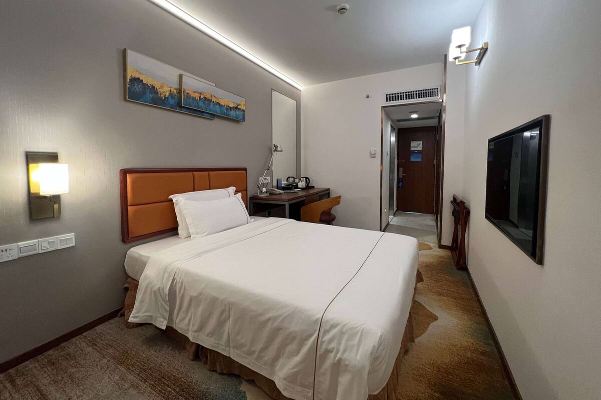 A hotel room with a large bed, a desk, a chair, a TV, and artwork on the wall.