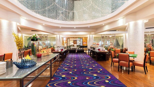 A spacious hotel lobby with a central dining area, multiple seating arrangements, and a high ceiling with decorative lighting. - Days Inn Guangzhou (Guangzhou)