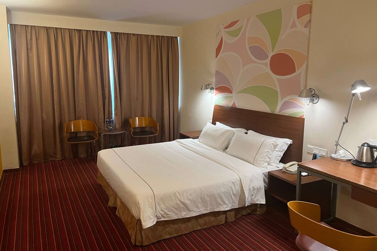 A hotel room with a large bed, two bedside tables, a desk, and a chair.