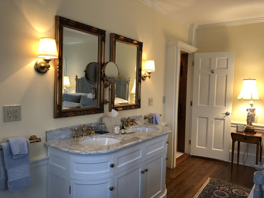 Une salle de bain avec un meuble-lavabo à deux vasques, deux miroirs fixés au mur et une petite table avec une lampe.