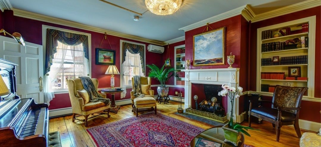 A room with a piano, two armchairs, a fireplace, and a bookshelf.