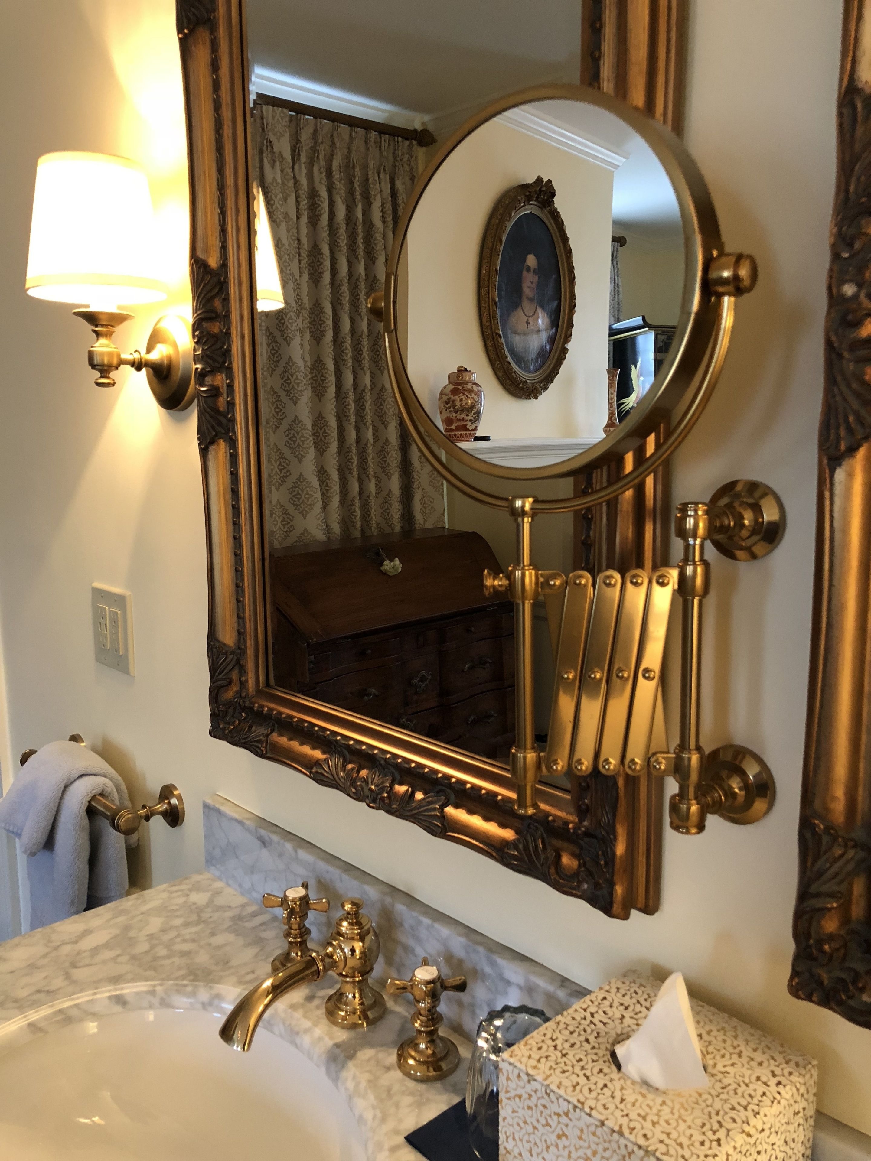 A bathroom with a large ornate mirror, a marble sink with gold fixtures, and a towel rack.