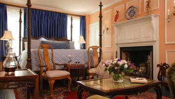A traditional bedroom with a four-poster bed, a fireplace, and a sitting area with a table and chairs.
